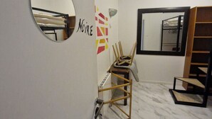 Una habitación con una cama individual superpuesta, un espejo, una silla de madera, una ventana y una estantería.