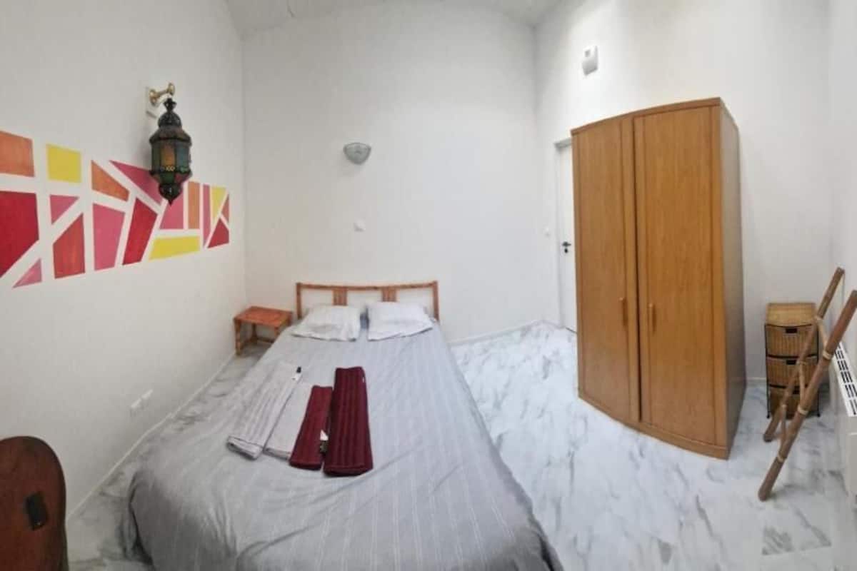 Quarto com cama, guarda-roupa, mesa de cabeceira e um adorno na parede.