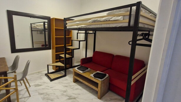 Una habitación compacta con una cama litera, un sofá rojo, un escritorio de madera y una silla.