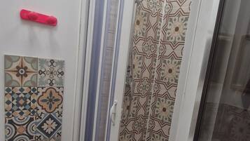 Ducha con puerta de vidrio, azulejos decorativos en las paredes y un picaporte rojo.