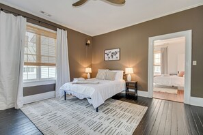 A bedroom with a bed, two bedside lamps, a world map on the wall, and a view into another room.