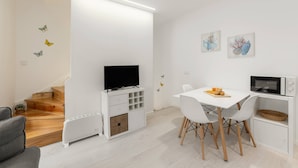 A modern living room with a flat-screen TV, dining table, and chairs. There is a staircase with wooden steps and a white cabinet with drawers. - Fly House Nazaré - 3 minute walk to the beach (Nazaré)