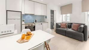 A modern kitchen with white cabinets, a dining table with a breakfast setup, and a grey sofa with patterned cushions. - Fly House Nazaré - 3 minute walk to the beach (Nazaré)