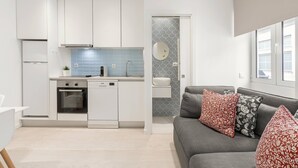 A modern kitchen with white cabinets, a built-in oven, and a dishwasher. There is a grey sofa with red and black patterned cushions in the living area. - Fly House Nazaré - 3 minute walk to the beach (Nazaré)