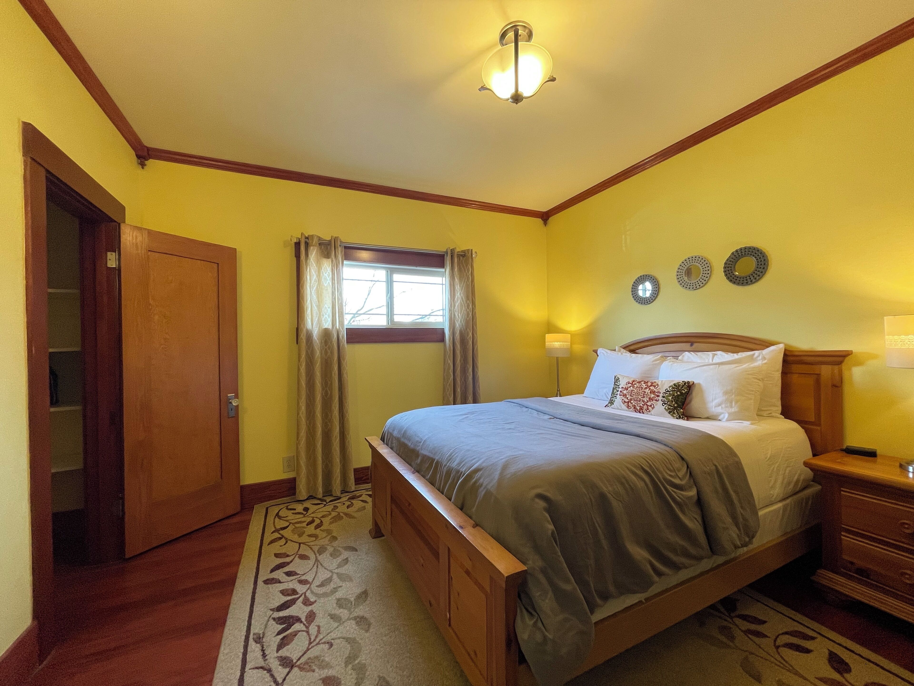A bedroom with a wooden bed, a nightstand, a lamp, a window with curtains, and a door.