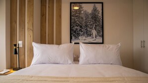 A neatly made bed with white linens and pillows, a wooden headboard, a framed picture of a snowy landscape, and a bedside table with a lamp and a book. - Barron by Wynwood House  (Lima)