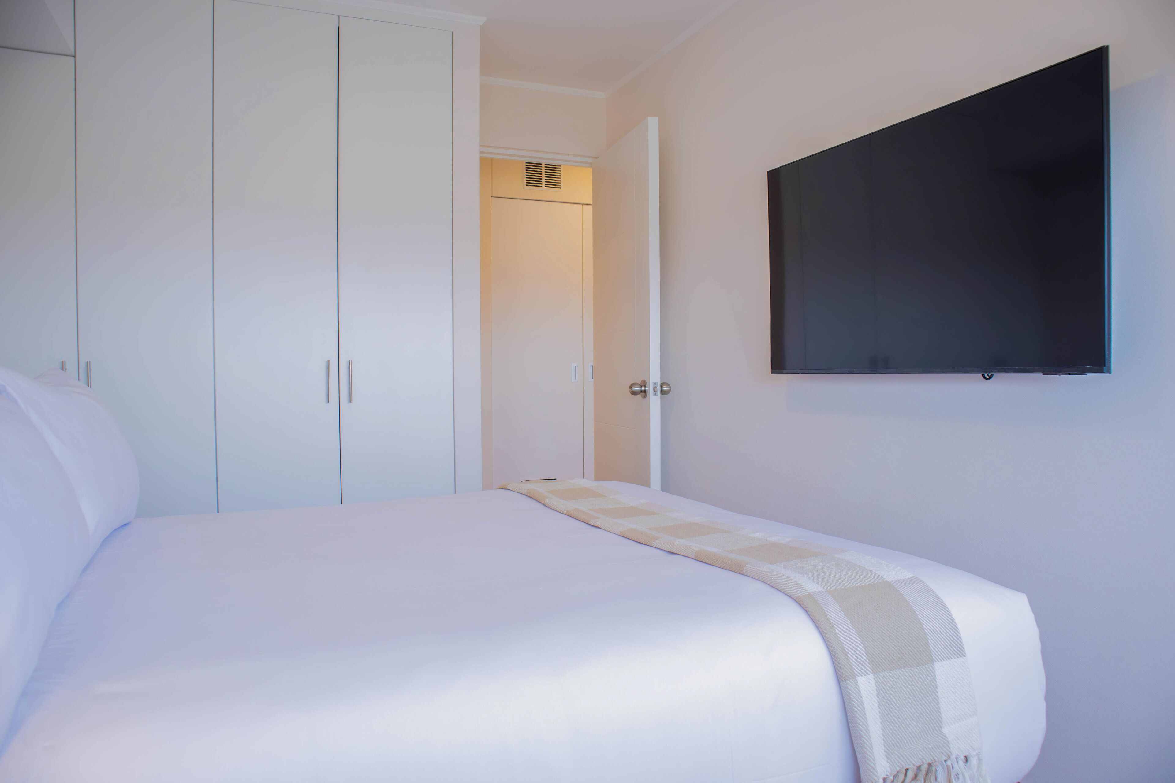 Quarto com cama, guarda-roupa e televisão fixada na parede.