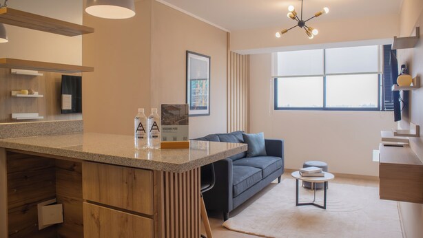 A modern kitchen with a wooden island, a grey sofa, and a small round table. - Barron by Wynwood House  (Lima)