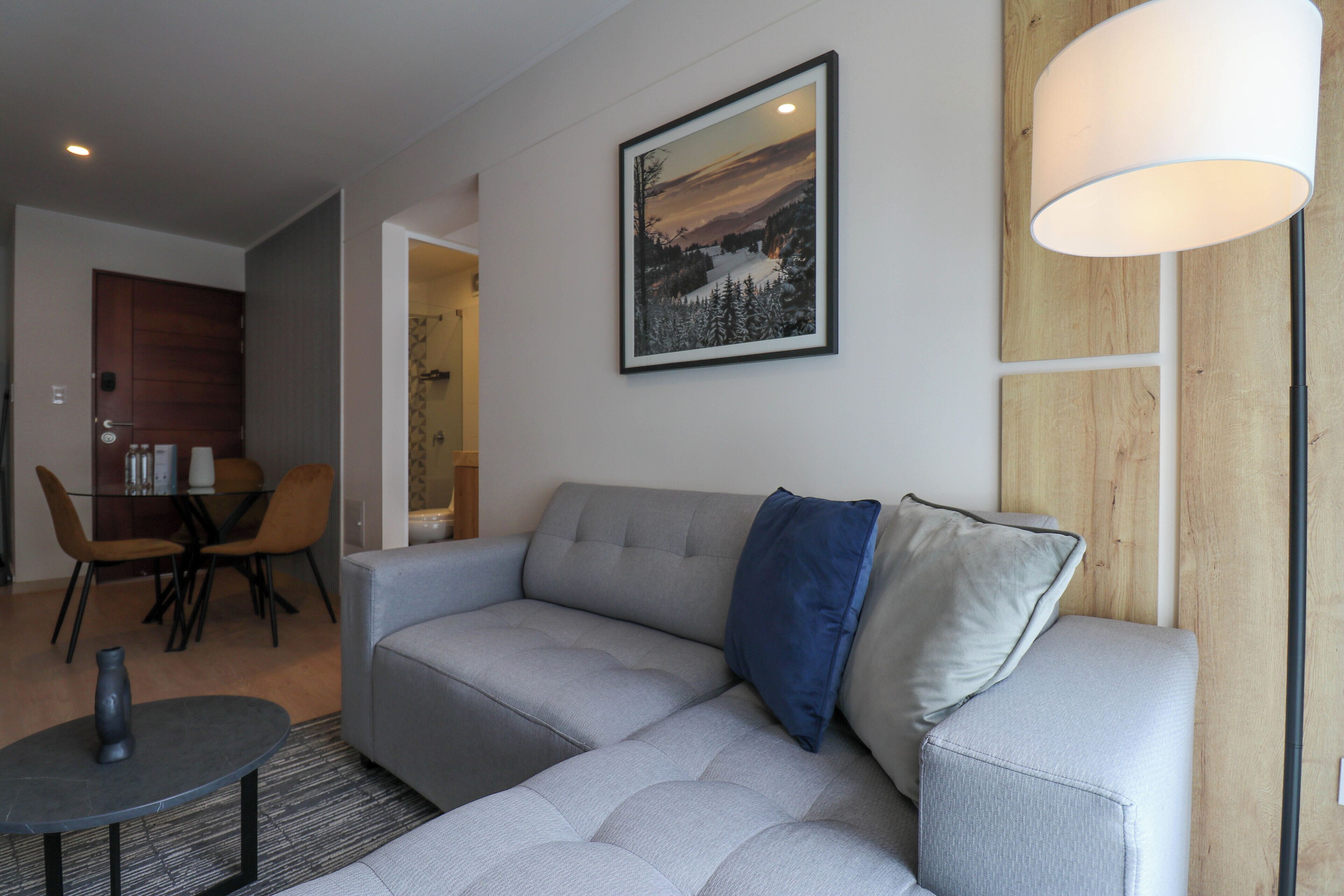 Uma sala de estar moderna com um sofá cinza, uma mesa de centro redonda e uma área de jantar com mesa e cadeiras de madeira.