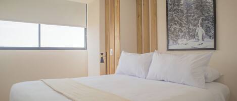 A bedroom with a large bed, a window, wooden paneling, and a framed picture on the wall.