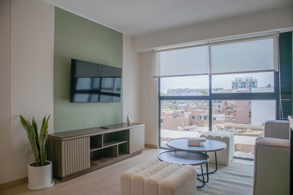 Una sala de estar moderna con un televisor de pantalla plana, una planta en maceta, un mueble de madera para entretenimiento, una mesa de centro redonda y un sofá.