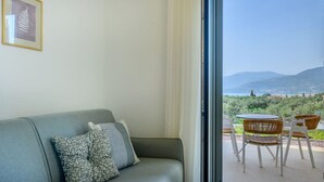 Una habitación con un sofá gris, una obra de arte con una hoja enmarcada y vistas a un paisaje montañoso a través de un ventanal.