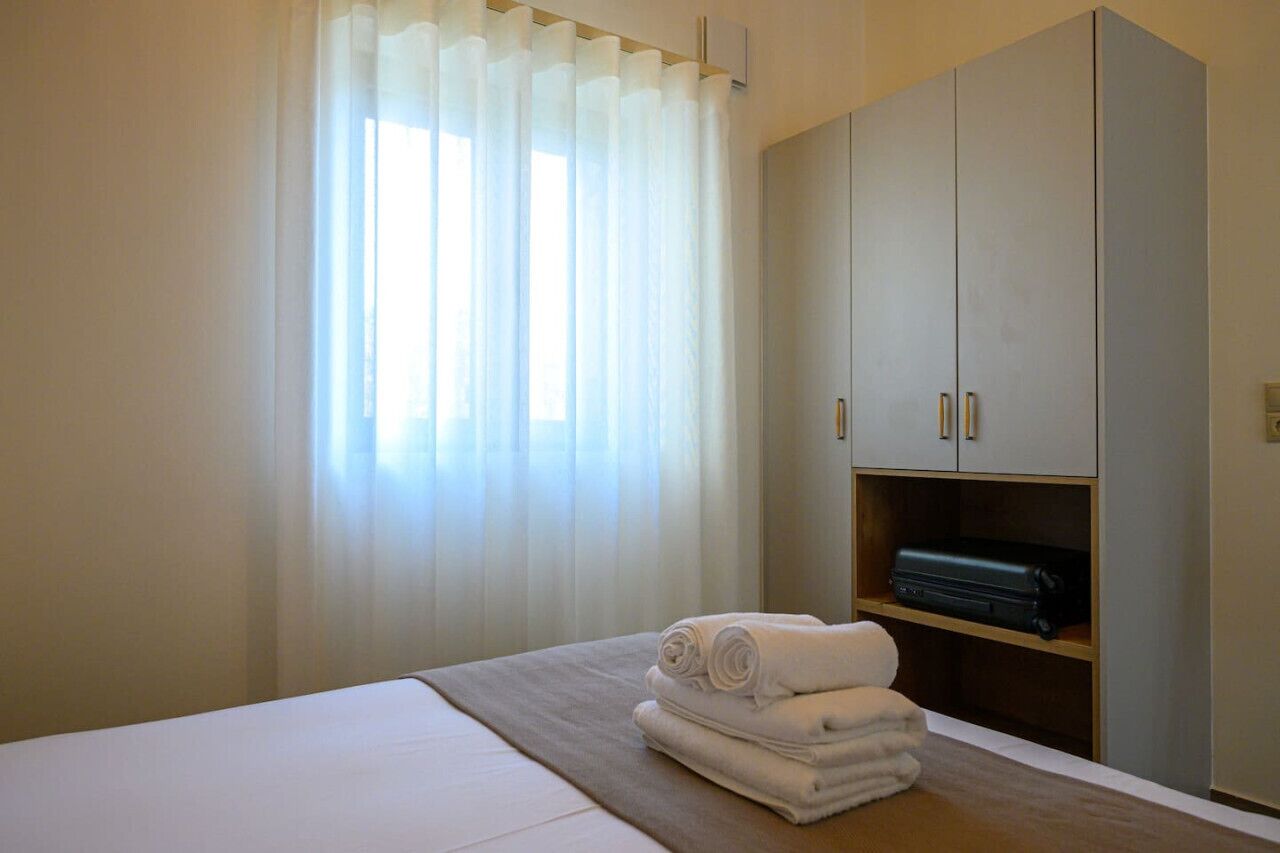 A hotel room with a bed, a wardrobe, and a suitcase on a shelf.