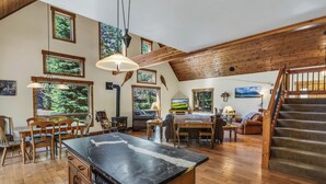 A spacious living area with a wooden staircase, large windows, and a central island with a black countertop. - Beautiful 3 Bedroom Mountain Paradise near Lake Davis (Portola)