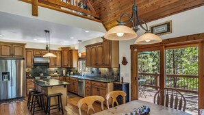 A spacious kitchen with wooden cabinets, a stainless steel refrigerator, and a large island with stools. - Beautiful 3 Bedroom Mountain Paradise near Lake Davis (Portola)