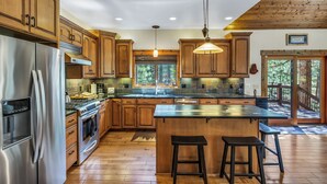 A spacious kitchen with wooden cabinets, stainless steel appliances, and a large island with stools. - Beautiful 3 Bedroom Mountain Paradise near Lake Davis (Portola)