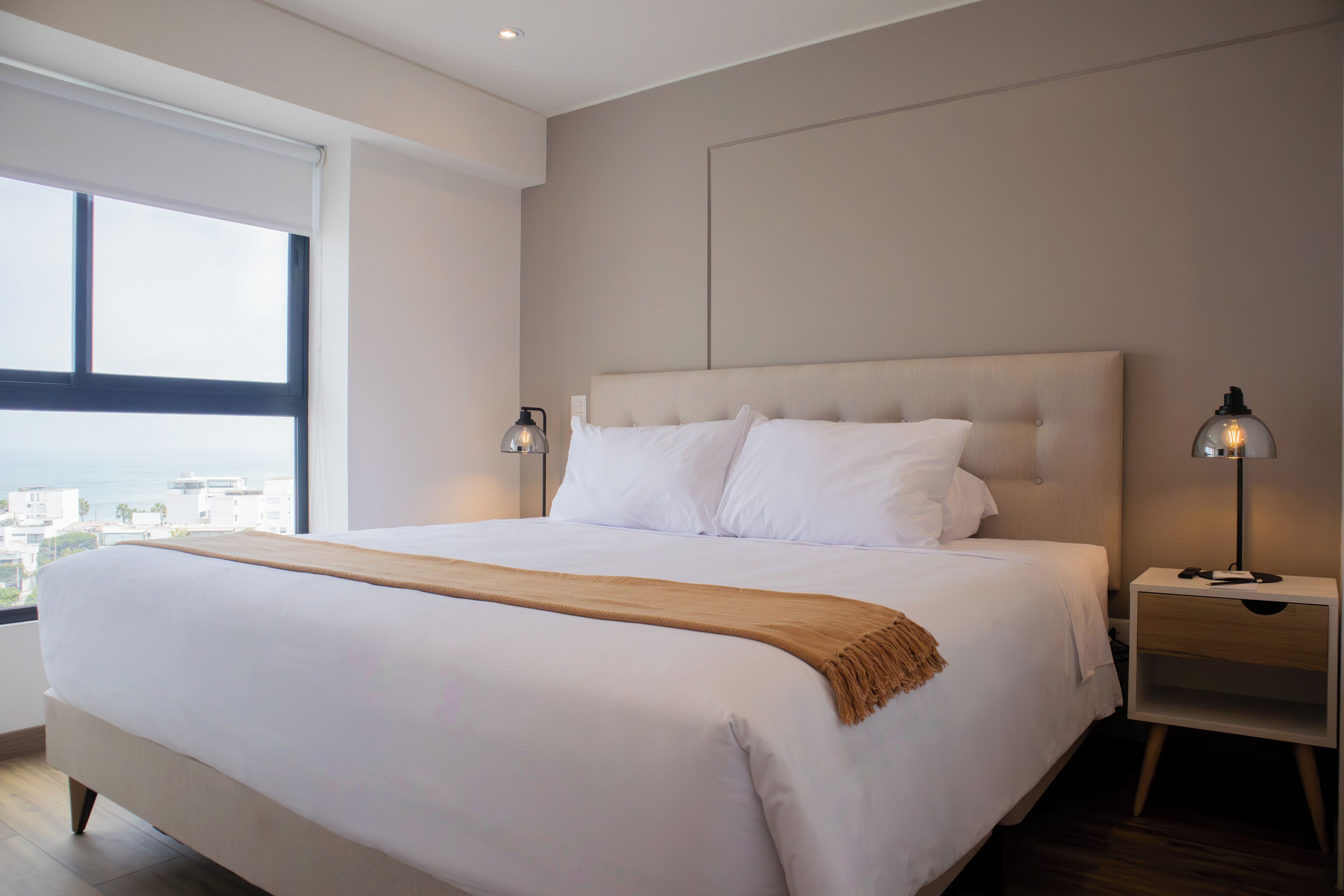A modern bedroom with a large bed, two bedside tables, and a view of the city.