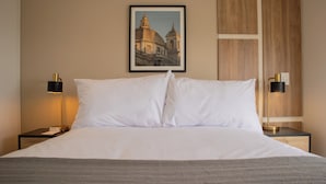 A neatly made bed with white linens, a framed picture of a building on the wall, and two bedside tables with lamps. - Aquilaria by Wynwood House  (Lima)