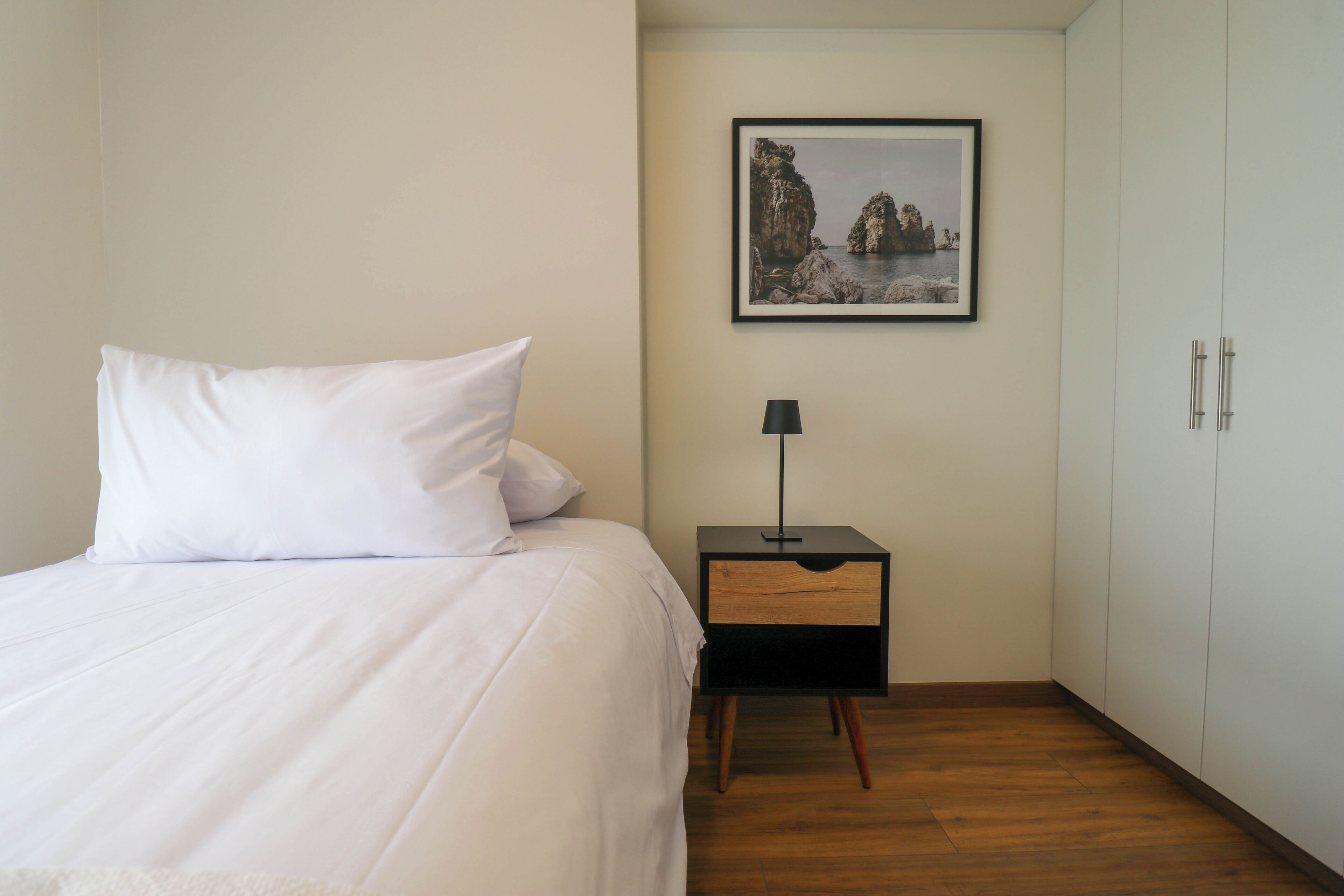 Une chambre à coucher avec un lit, une table de chevet, une lampe, une armoire et un tableau encadré au mur.