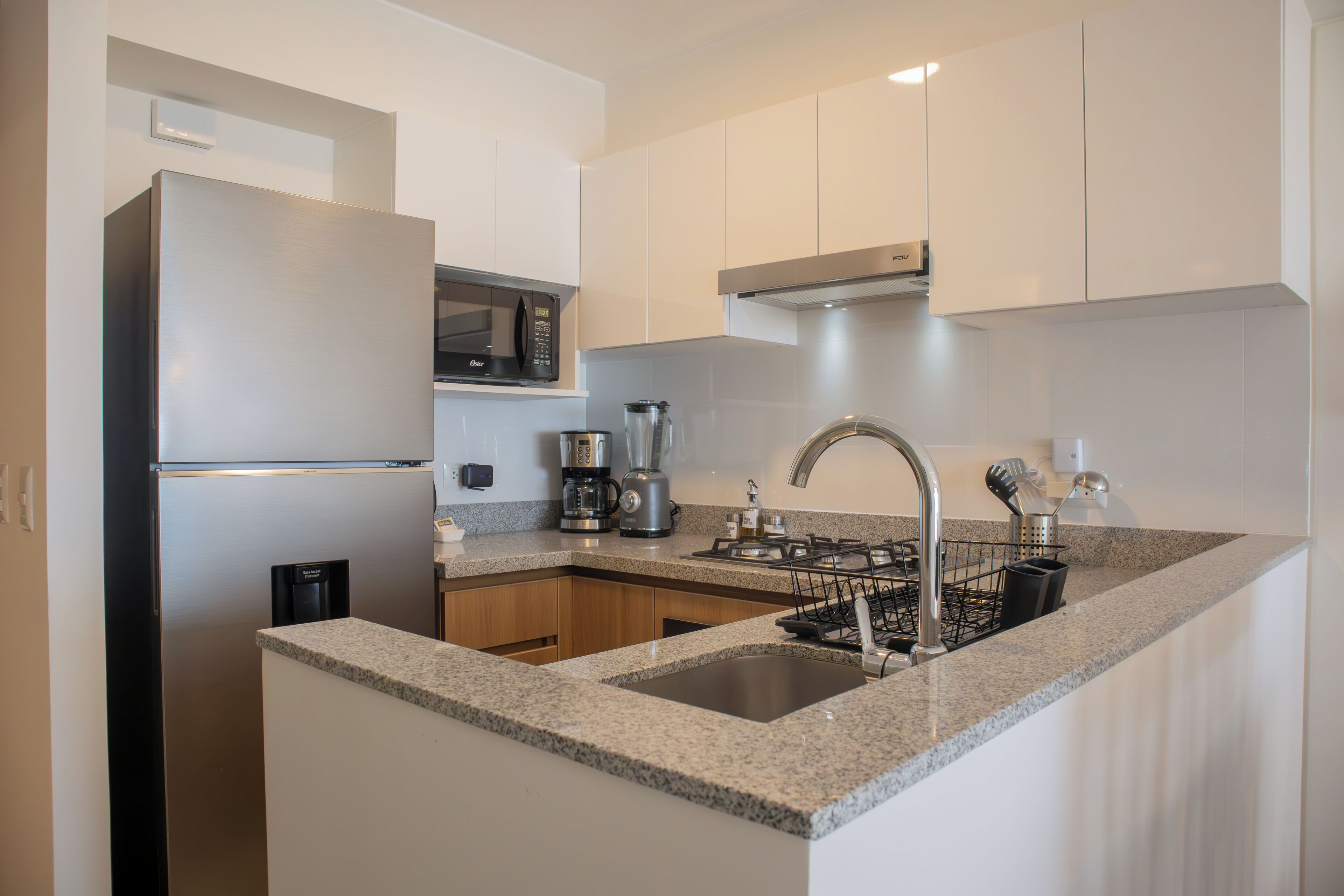 Una cucina moderna con frigorifero in acciaio inox, forno a microonde integrato, macchina da caffè e piano cottura a gas.