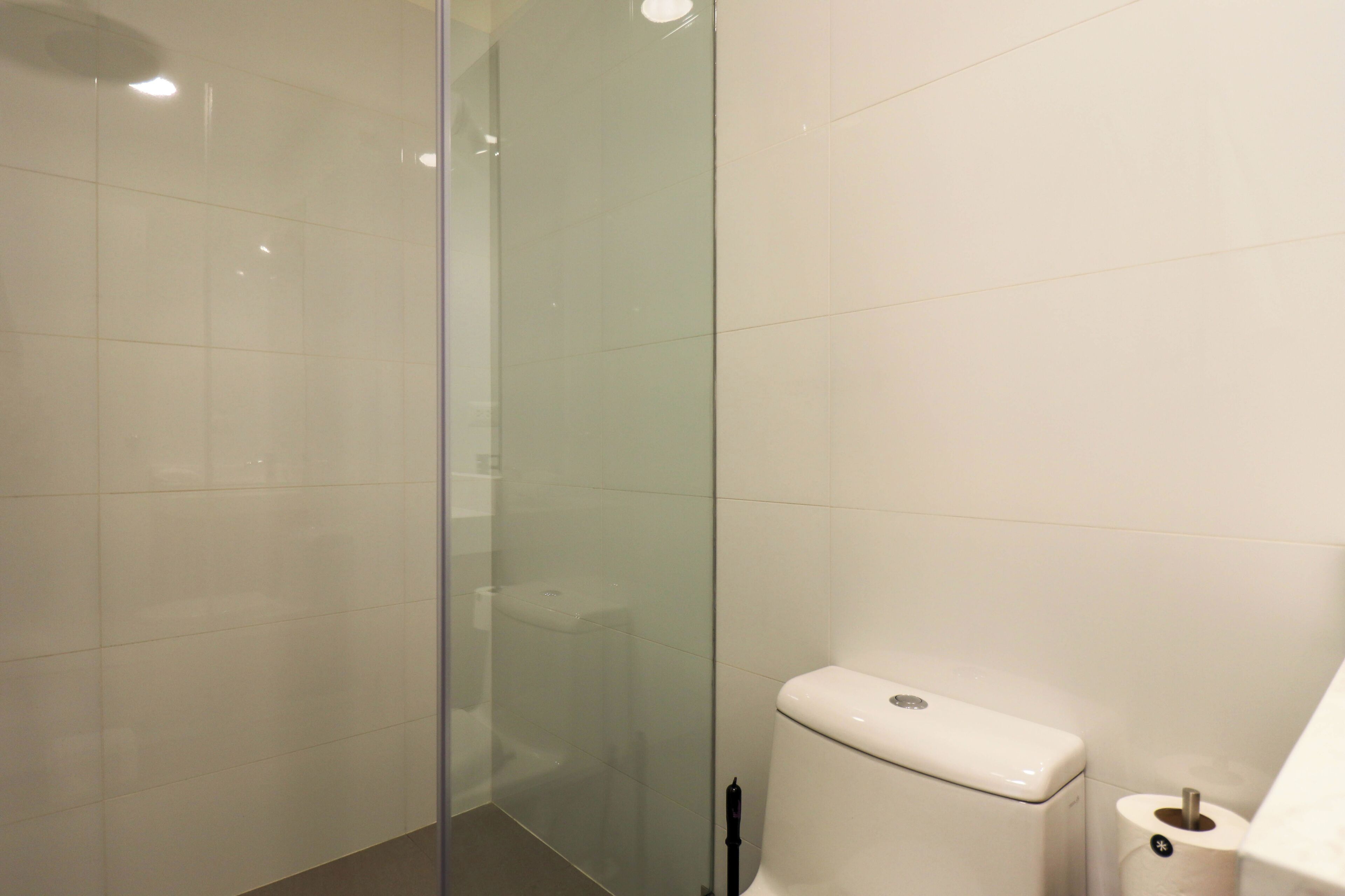 Une salle de bain avec une douche à parois de verre, des toilettes et un rouleau de papier toilette posé sur le sol.