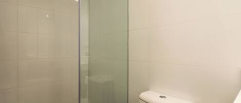 Une salle de bain avec une douche à parois de verre, des toilettes et un rouleau de papier toilette posé sur le sol.
