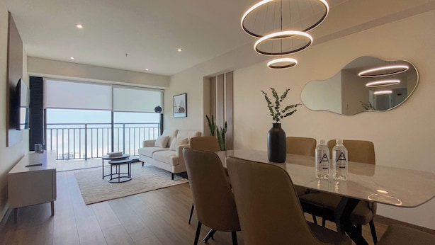 A modern living room with a dining table, chairs, a sofa, and a large window with a view. - Aquilaria by Wynwood House  (Lima)