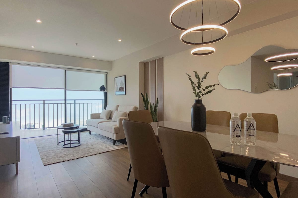 A modern living room with a dining table, chairs, a sofa, and a large window with a view.