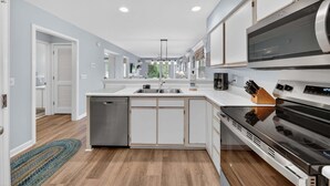 A modern kitchen with a dishwasher, stove, microwave, and a large island with a sink.