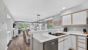 A modern kitchen with white cabinetry, a dishwasher, and a dining area with a bench and table.