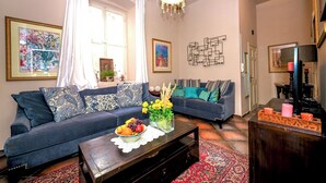 A living room with two sofas, a coffee table with fruit, a chandelier, and artwork on the walls.