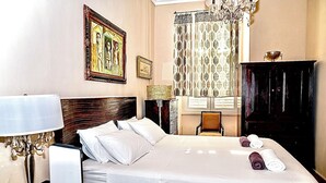 A hotel room with a large bed, a desk, a chair, a wardrobe, and a chandelier.