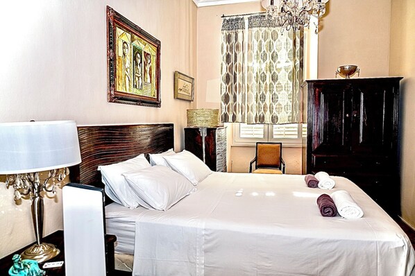 A hotel room with a large bed, a desk, a chair, a wardrobe, and a chandelier.