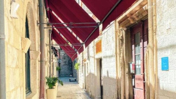 A narrow stone-paved alley with red awnings over the buildings.