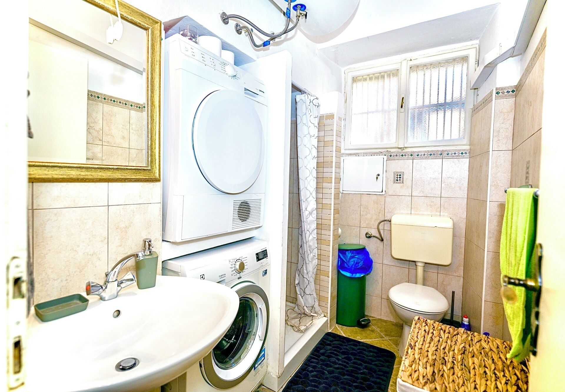 A compact bathroom with a washing machine, a sink, a toilet, and a shower area.