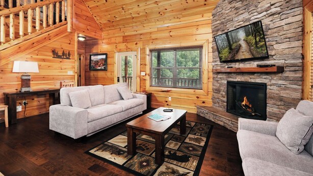 A cozy log cabin interior with a fireplace, wooden walls, a sofa, and a dining table. - Time Well Spent - 10 Minutes from Parkway Attractions, Shops, Events & Food (Sevierville)