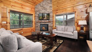 A cozy cabin interior with a stone fireplace, wooden walls, and a comfortable seating area. - Time Well Spent - 10 Minutes from Parkway Attractions, Shops, Events & Food (Sevierville)