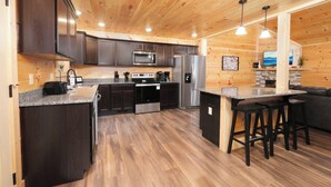 A modern kitchen with dark cabinets, stainless steel appliances, and a wooden floor.