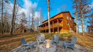 A cabin with a deck and a fire pit surrounded by Adirondack chairs.