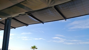 A table with food items and a laptop, overlooking a beach with a palm tree and the ocean. - Exceptional sea view, air conditioning, parking, private beaches, swimming pools, tennis court, marina. (Bandol)