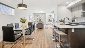 Una cocina moderna con una isla central, asientos tipo bar y un comedor con sillas y mesa.