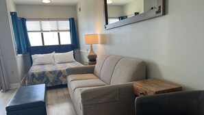 Una camera d'albergo con un letto, una poltrona, un poggiapiedi, un comodino e una lampada.