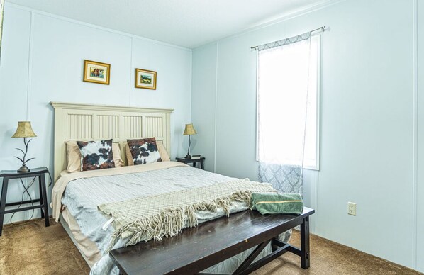 A bedroom with a bed, two bedside tables with lamps, a bench, and two framed pictures on the wall.