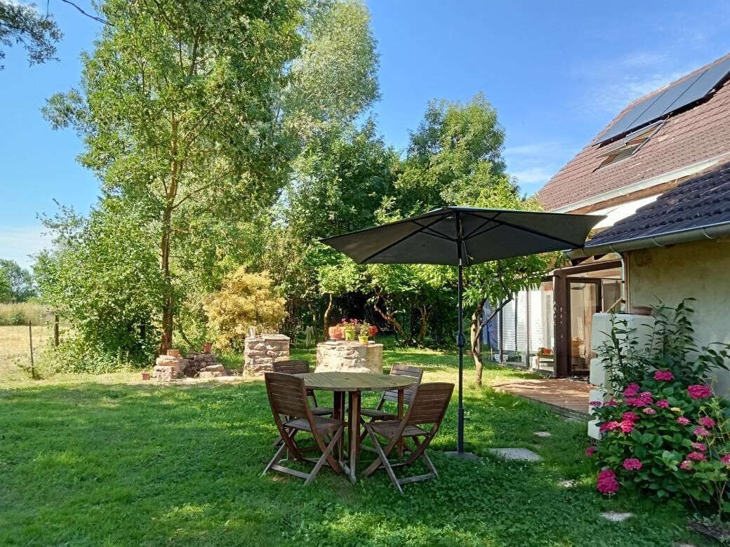 Un patio con una mesa y sillas, una estructura de piedra y una casa con techo inclinado.