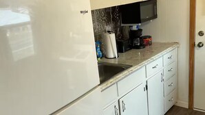 Una cocina con armarios blancos, un refrigerador blanco, un microondas y una cafetera.