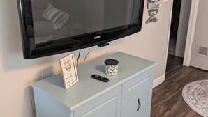 Un televisor de pantalla plana montado en un mueble azul claro, con un control remoto y una cita enmarcada encima.