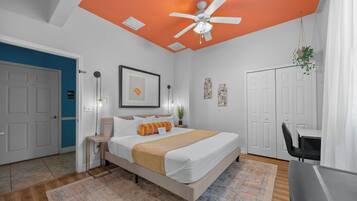 Une chambre à coucher comprenant un lit, des tables de chevet, un ventilateur de plafond et un bureau avec une chaise.