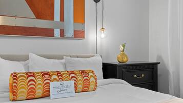 Una camera d'albergo con un letto, cuscini, un comodino, un vaso e un quadro appeso al muro.