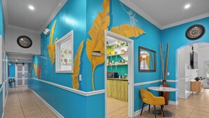 A brightly colored hallway with a large clock, a dining area with a yellow chair, and a kitchen visible through an open door. - Banana Leaf Villa (Orlando)