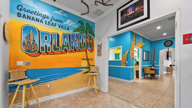 A room with a mural of Orlando, a wooden stool, a chair, and a tiled floor. - Banana Leaf Villa (Orlando)